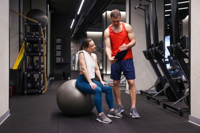 Photo of Young woman with professional personal trainer in gym