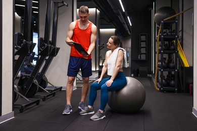 Photo of Young woman with professional personal trainer in gym