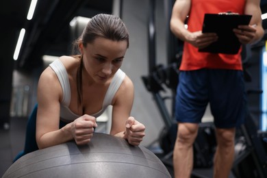 Photo of Young woman exercising with fitness ball near professional personal trainer in gym