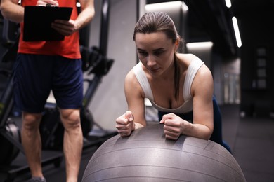 Photo of Young woman exercising with fitness ball near professional personal trainer in gym