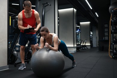 Photo of Young woman exercising with fitness ball near professional personal trainer in gym, space for text