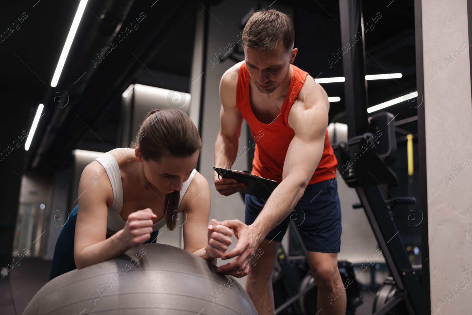 Young woman exercising with fitness ball near professional personal trainer in gym Photo of Young woman exercising with fitness ball near professional personal trainer in gym