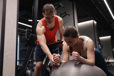 Photo of Young woman exercising with fitness ball near professional personal trainer in gym