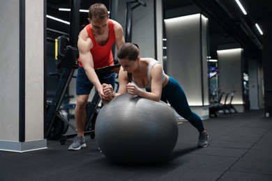 Photo of Young woman exercising with fitness ball near professional personal trainer in gym