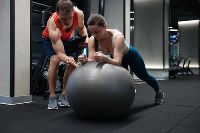 Photo of Young woman exercising with fitness ball near professional personal trainer in gym