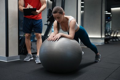 Photo of Young woman exercising with fitness ball near professional personal trainer in gym
