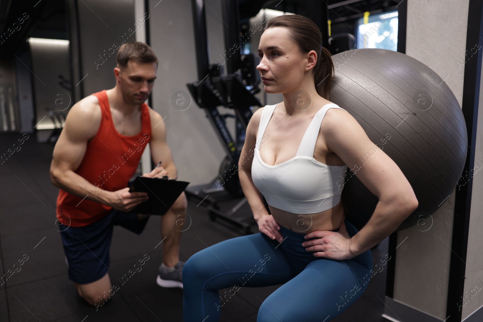 Young woman exercising with fitness ball near professional personal trainer in gym Photo of Young woman exercising with fitness ball near professional personal trainer in gym