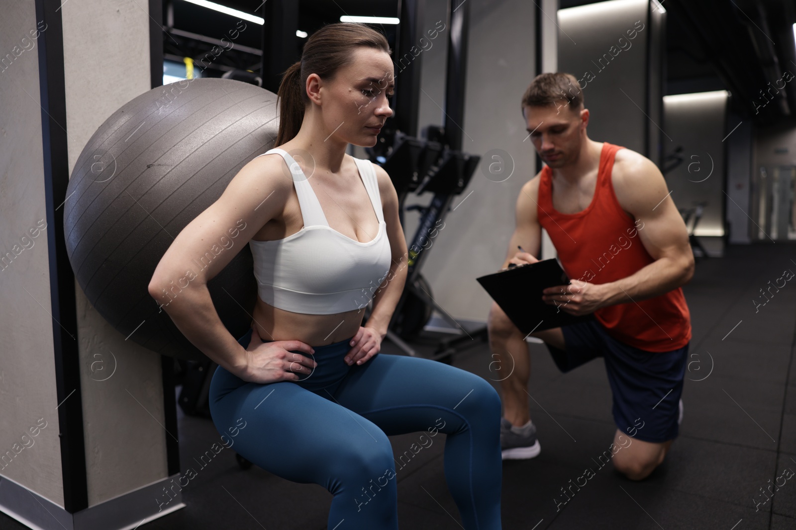 Young woman exercising with fitness ball near professional personal trainer in gym Photo of Young woman exercising with fitness ball near professional personal trainer in gym
