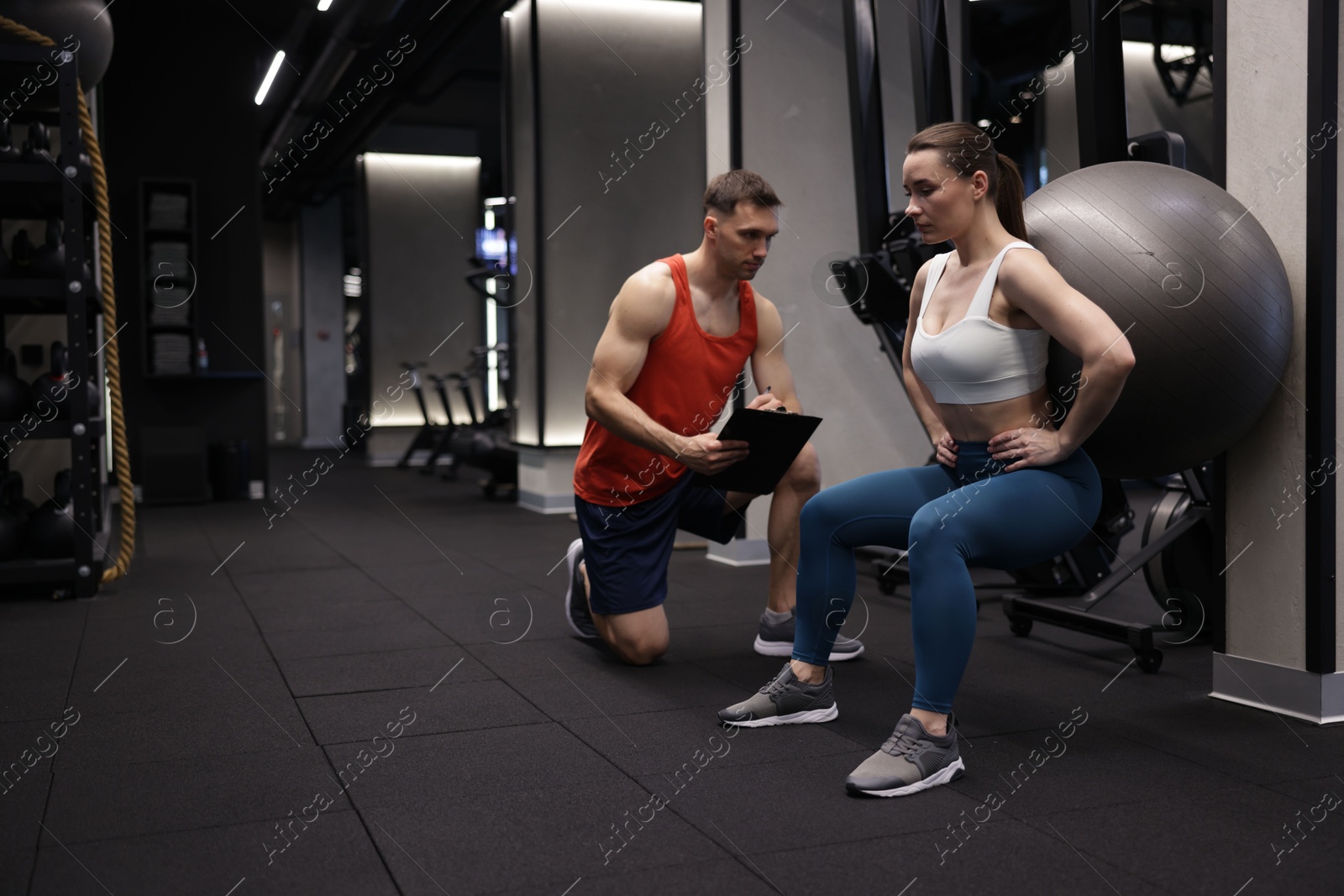 Young woman exercising with fitness ball near professional personal trainer in gym, space for text Photo of Young woman exercising with fitness ball near professional personal trainer in gym, space for text