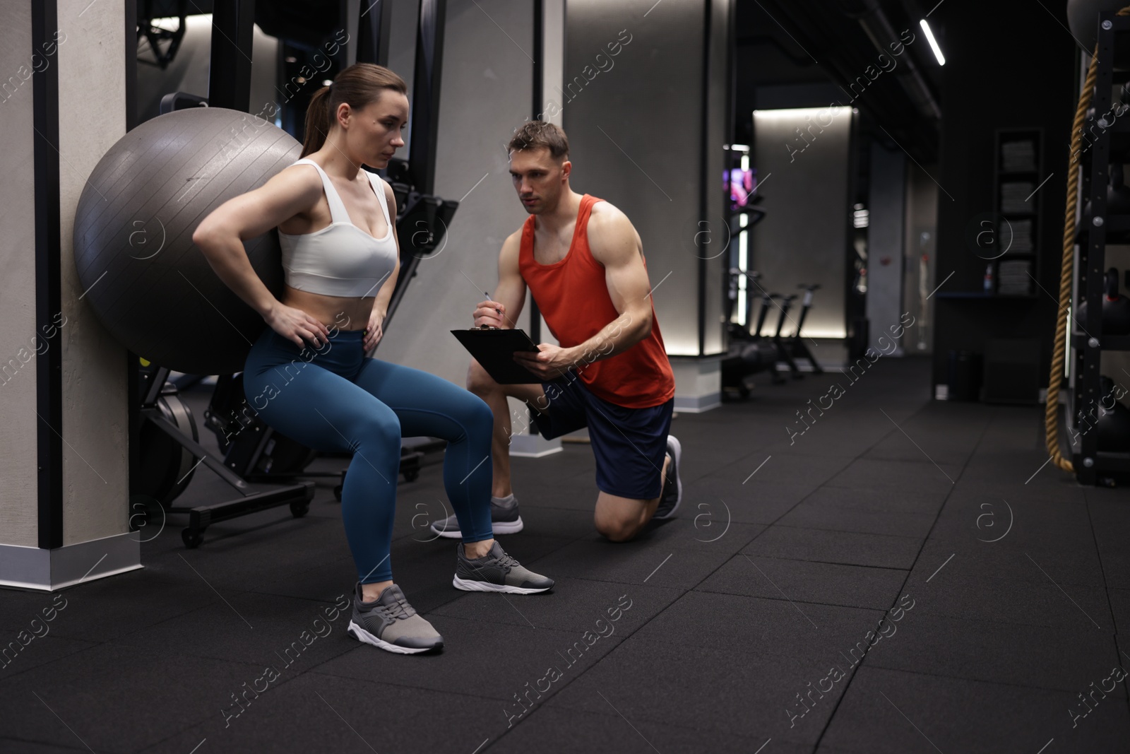 Young woman exercising with fitness ball near professional personal trainer in gym, space for text Photo of Young woman exercising with fitness ball near professional personal trainer in gym, space for text
