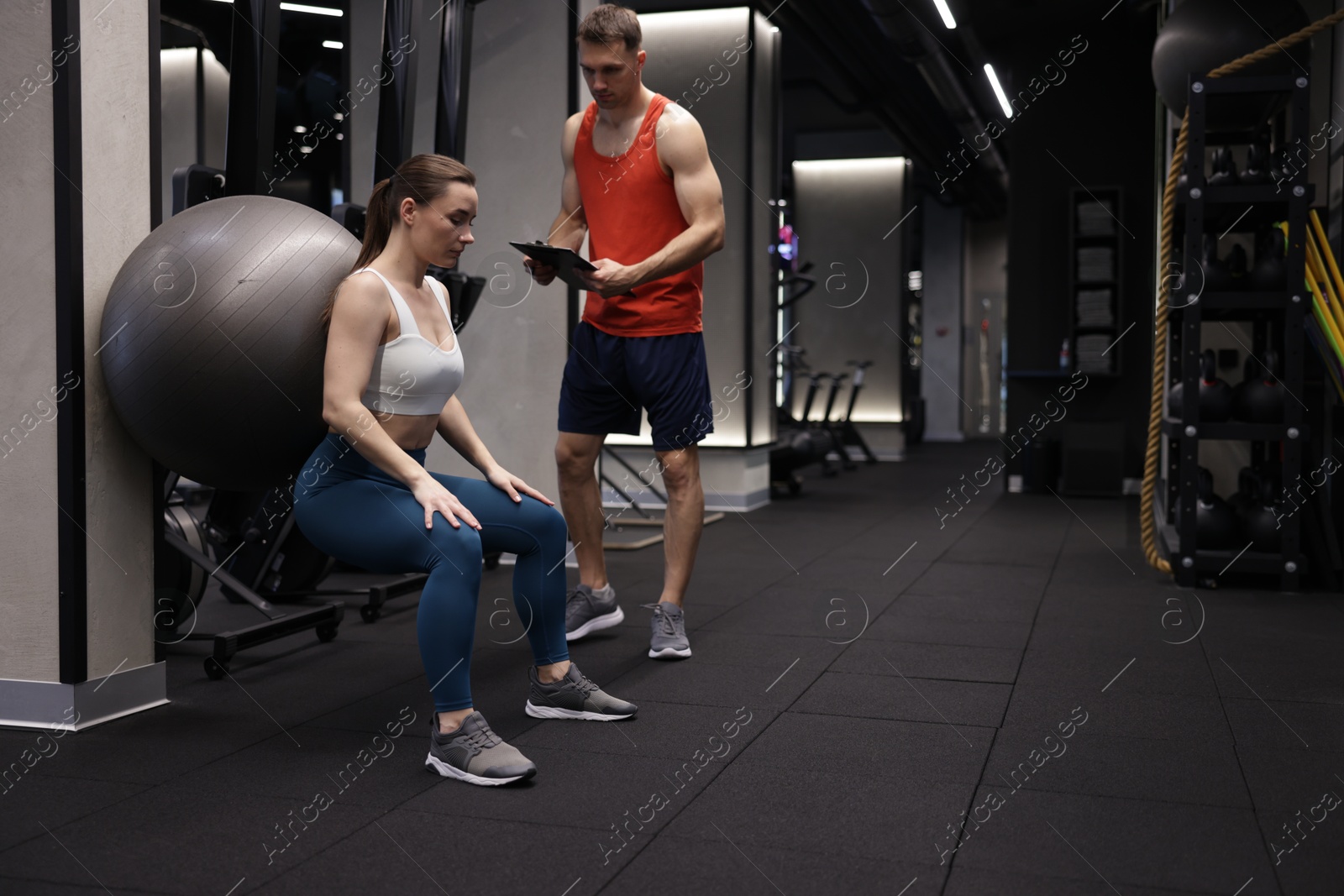 Young woman exercising with fitness ball near professional personal trainer in gym, space for text Photo of Young woman exercising with fitness ball near professional personal trainer in gym, space for text