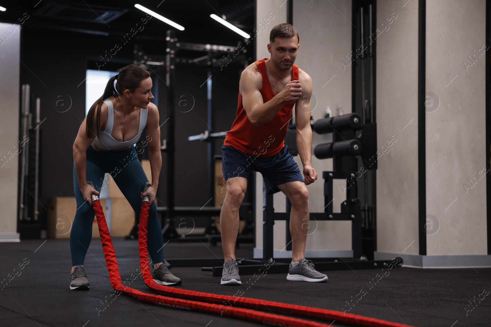Photo of Young woman exercising with battle ropes and professional personal trainer in gym