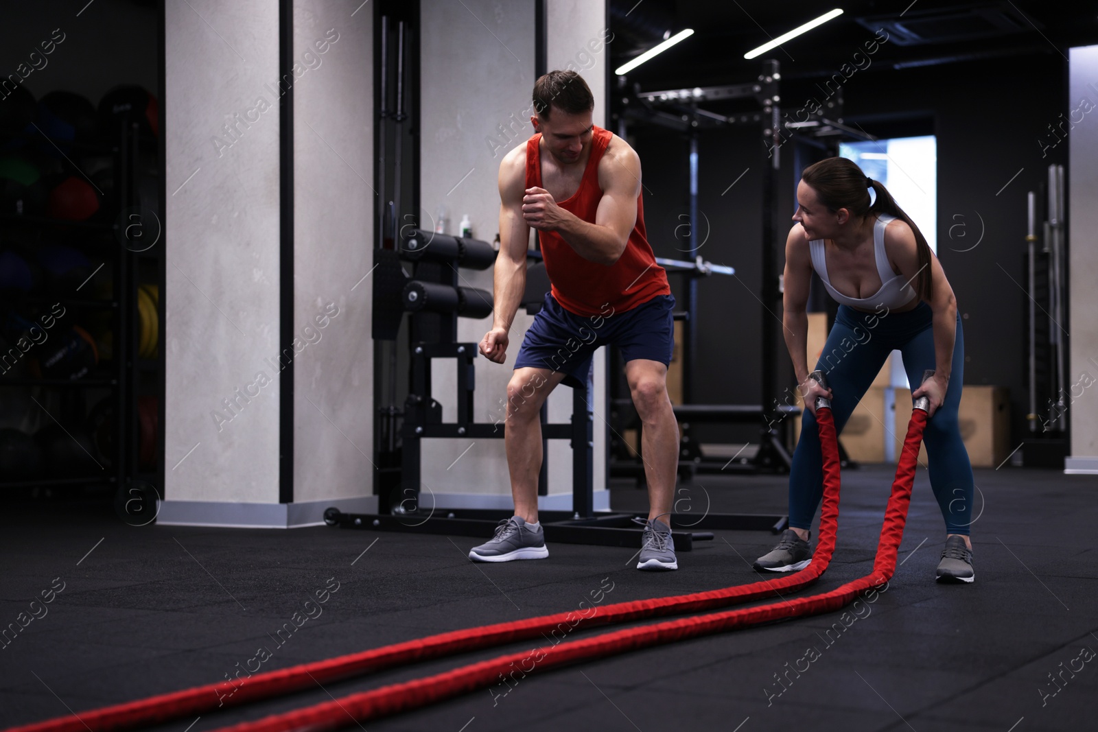 Photo of Young woman exercising with battle ropes and professional personal trainer in gym