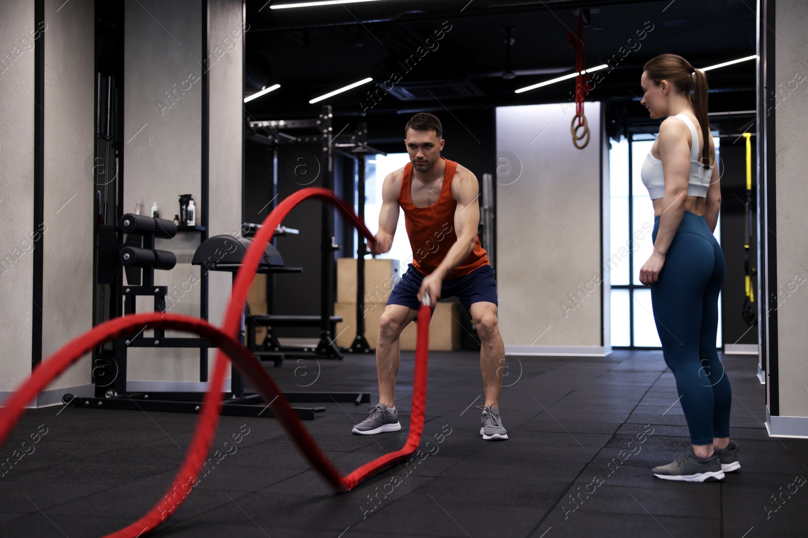 Professional personal trainer showing young woman how to exercise with battle ropes in gym Photo of Professional personal trainer showing young woman how to exercise with battle ropes in gym