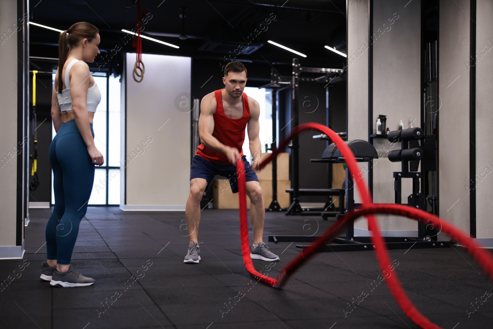 Professional personal trainer showing young woman how to exercise with battle ropes in gym Photo of Professional personal trainer showing young woman how to exercise with battle ropes in gym