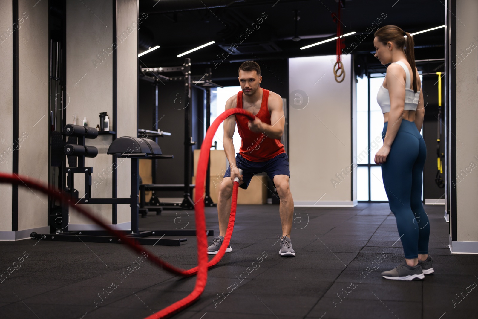 Professional personal trainer showing young woman how to exercise with battle ropes in gym Photo of Professional personal trainer showing young woman how to exercise with battle ropes in gym