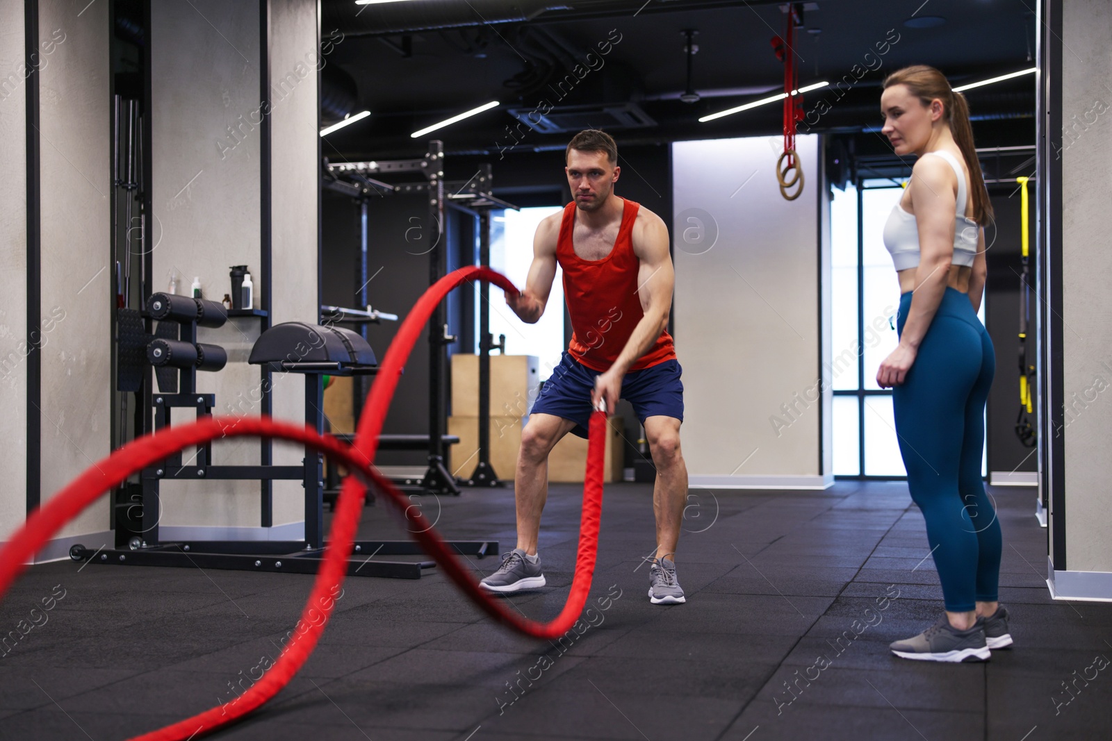 Professional personal trainer showing young woman how to exercise with battle ropes in gym Photo of Professional personal trainer showing young woman how to exercise with battle ropes in gym