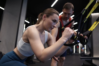 Photo of Young woman exercising with suspension trainers with professional personal coach in gym