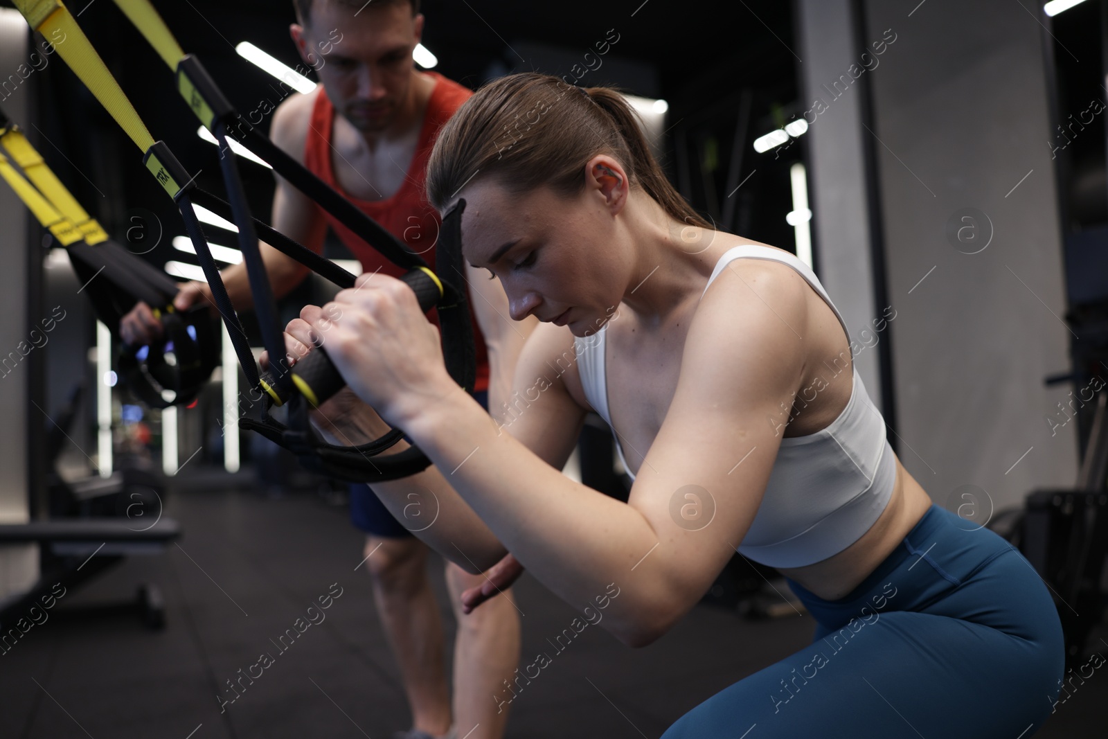 Young woman exercising with suspension trainers with professional personal coach in gym Photo of Young woman exercising with suspension trainers with professional personal coach in gym