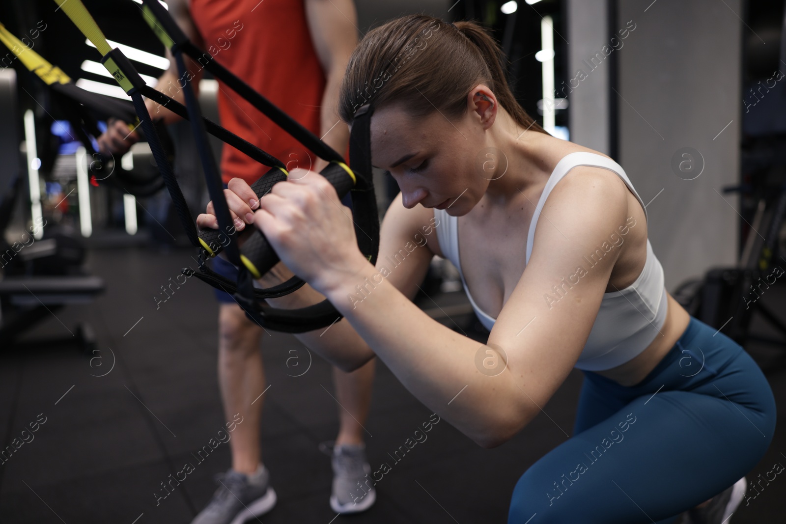 Young woman exercising with suspension trainers with professional personal coach in gym Photo of Young woman exercising with suspension trainers with professional personal coach in gym