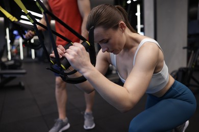 Photo of Young woman exercising with suspension trainers with professional personal coach in gym