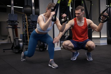 Photo of Young woman exercising with suspension trainers with professional personal coach in gym