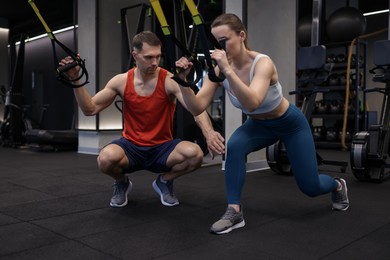 Photo of Young woman exercising with suspension trainers with professional personal coach in gym