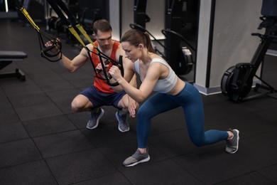 Photo of Young woman exercising with suspension trainers with professional personal coach in gym