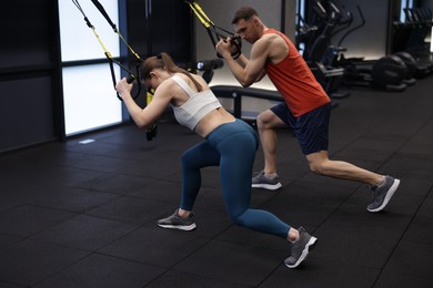 Photo of Young woman exercising with suspension trainers with professional personal coach in gym