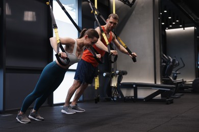 Photo of Young woman exercising with suspension trainers with professional personal coach in gym, space for text