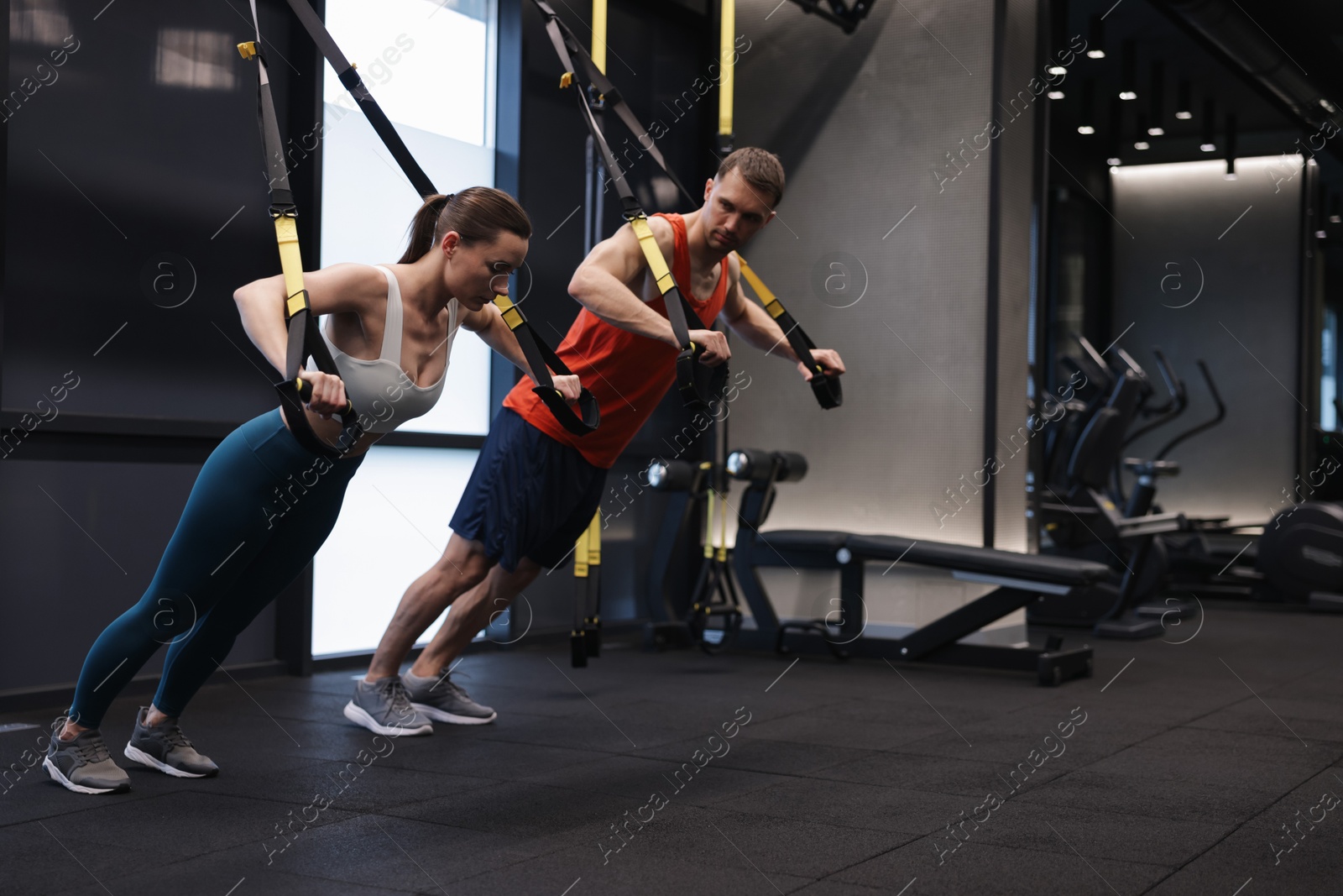 Young woman exercising with suspension trainers with professional personal coach in gym, space for text Photo of Young woman exercising with suspension trainers with professional personal coach in gym, space for text