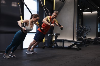 Photo of Young woman exercising with suspension trainers with professional personal coach in gym, space for text