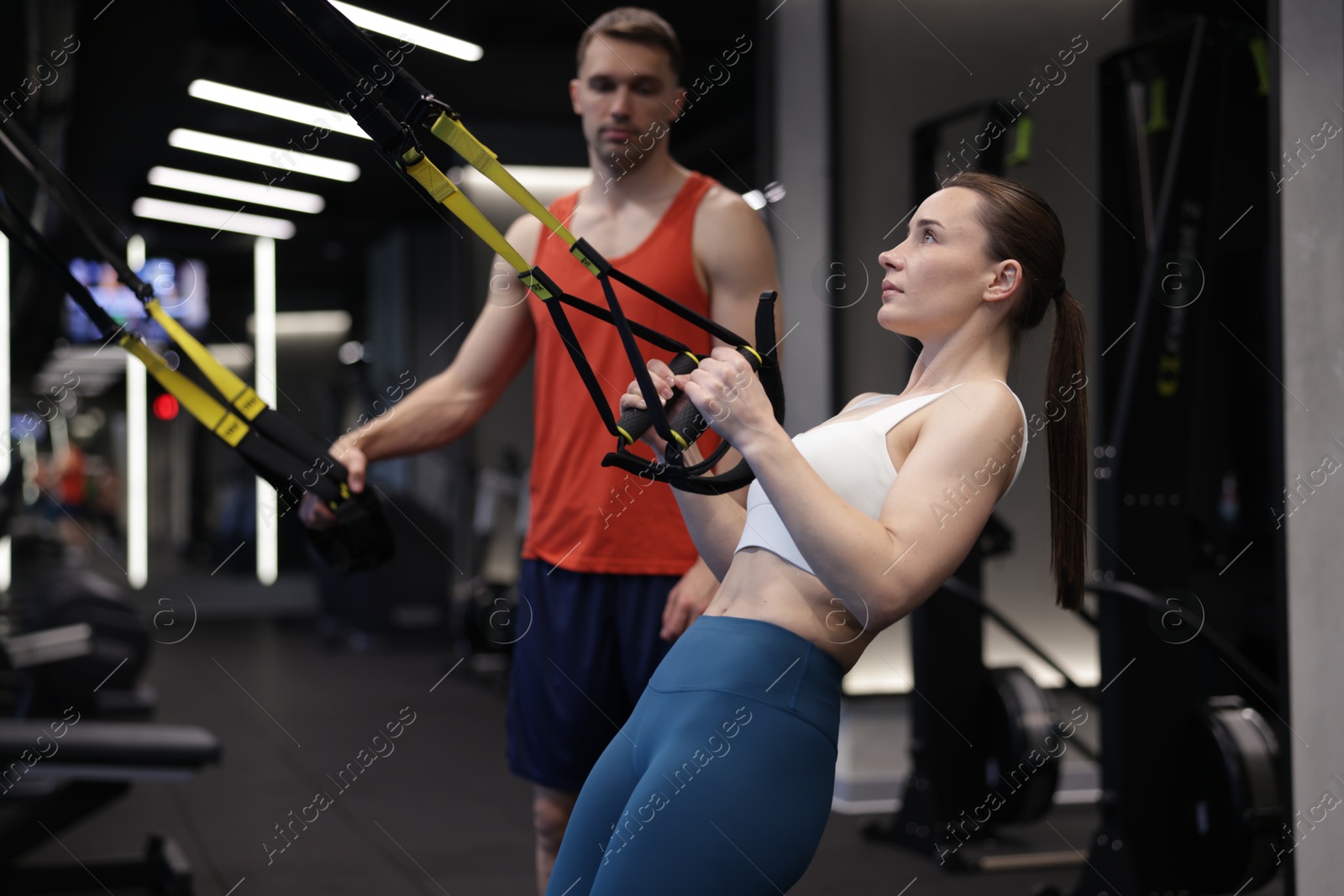 Young woman exercising with suspension trainers with professional personal coach in gym Photo of Young woman exercising with suspension trainers with professional personal coach in gym