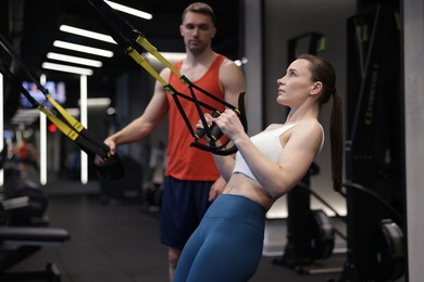 Photo of Young woman exercising with suspension trainers with professional personal coach in gym