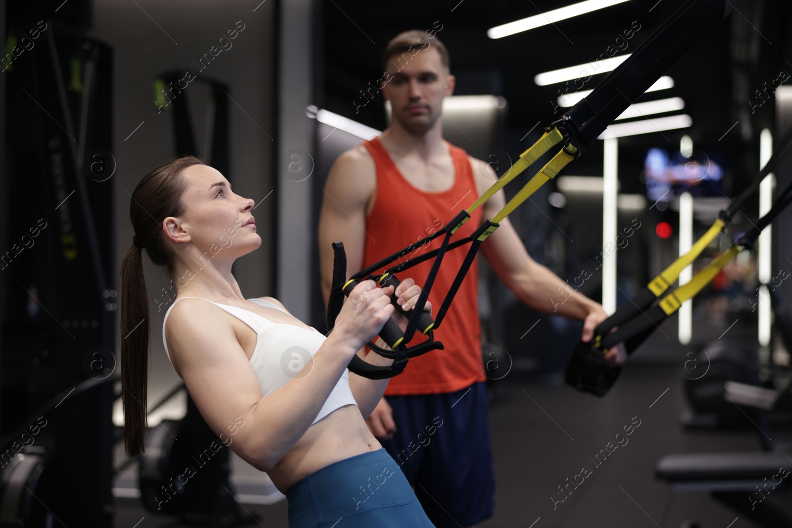 Young woman exercising with suspension trainers with professional personal coach in gym Photo of Young woman exercising with suspension trainers with professional personal coach in gym