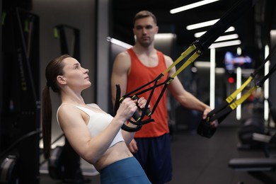 Photo of Young woman exercising with suspension trainers with professional personal coach in gym