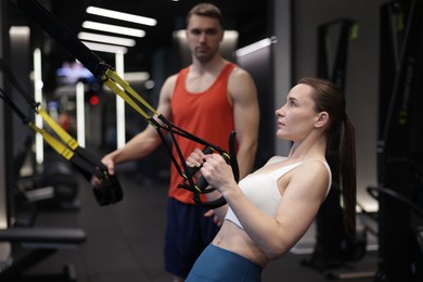 Photo of Young woman exercising with suspension trainers with professional personal coach in gym