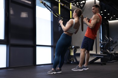 Photo of Young woman exercising with suspension trainers with professional personal coach in gym, space for text