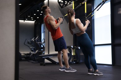 Photo of Young woman exercising with suspension trainers with professional personal coach in gym