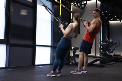Photo of Young woman exercising with suspension trainers with professional personal coach in gym, space for text