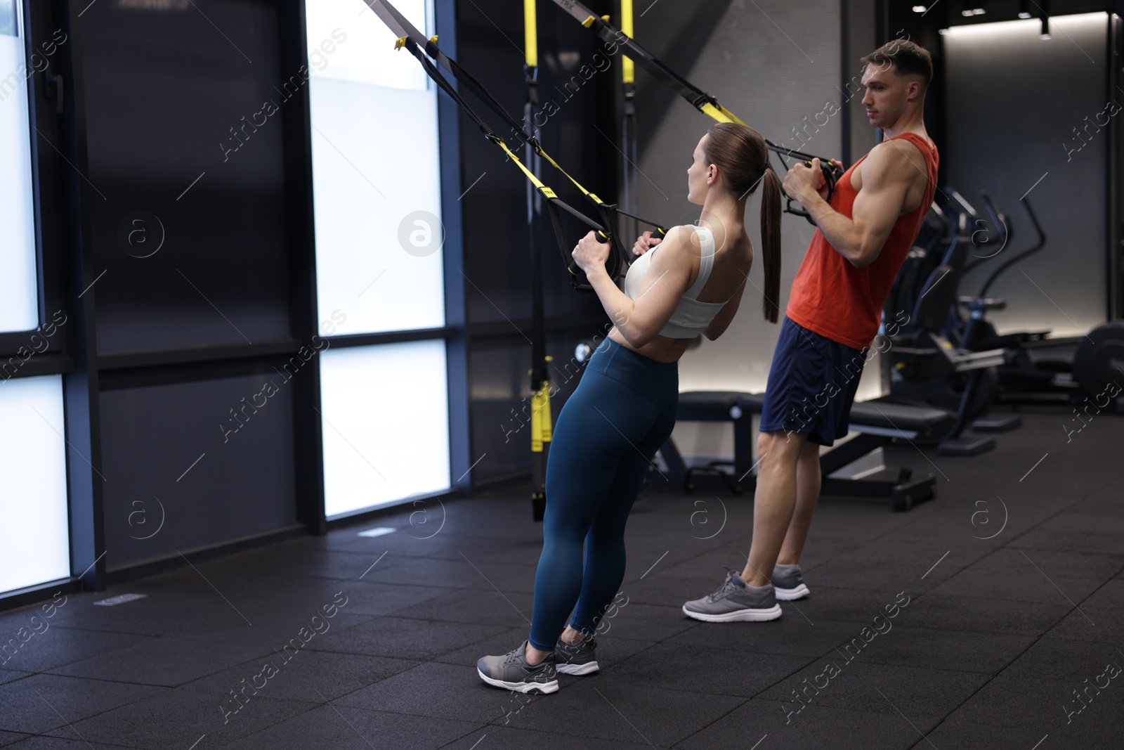 Young woman exercising with suspension trainers with professional personal coach in gym, space for text Photo of Young woman exercising with suspension trainers with professional personal coach in gym, space for text