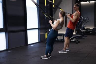Photo of Young woman exercising with suspension trainers with professional personal coach in gym, space for text