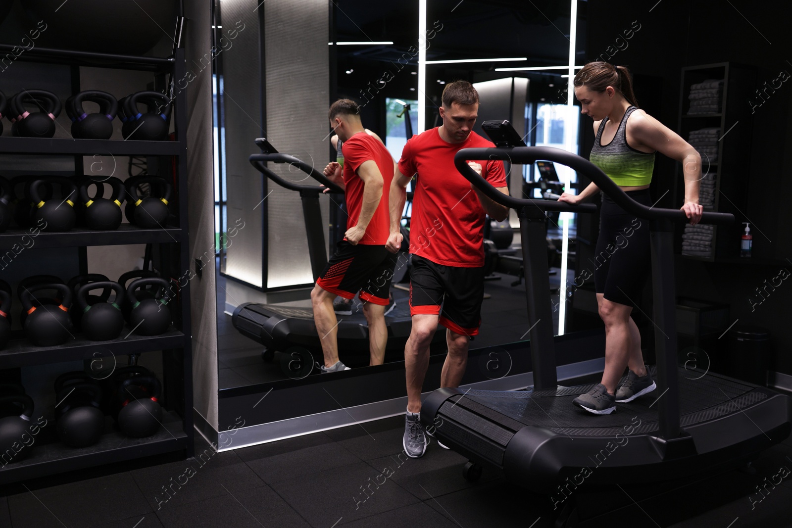 Photo of Young woman exercising on treadmill with professional personal trainer in gym