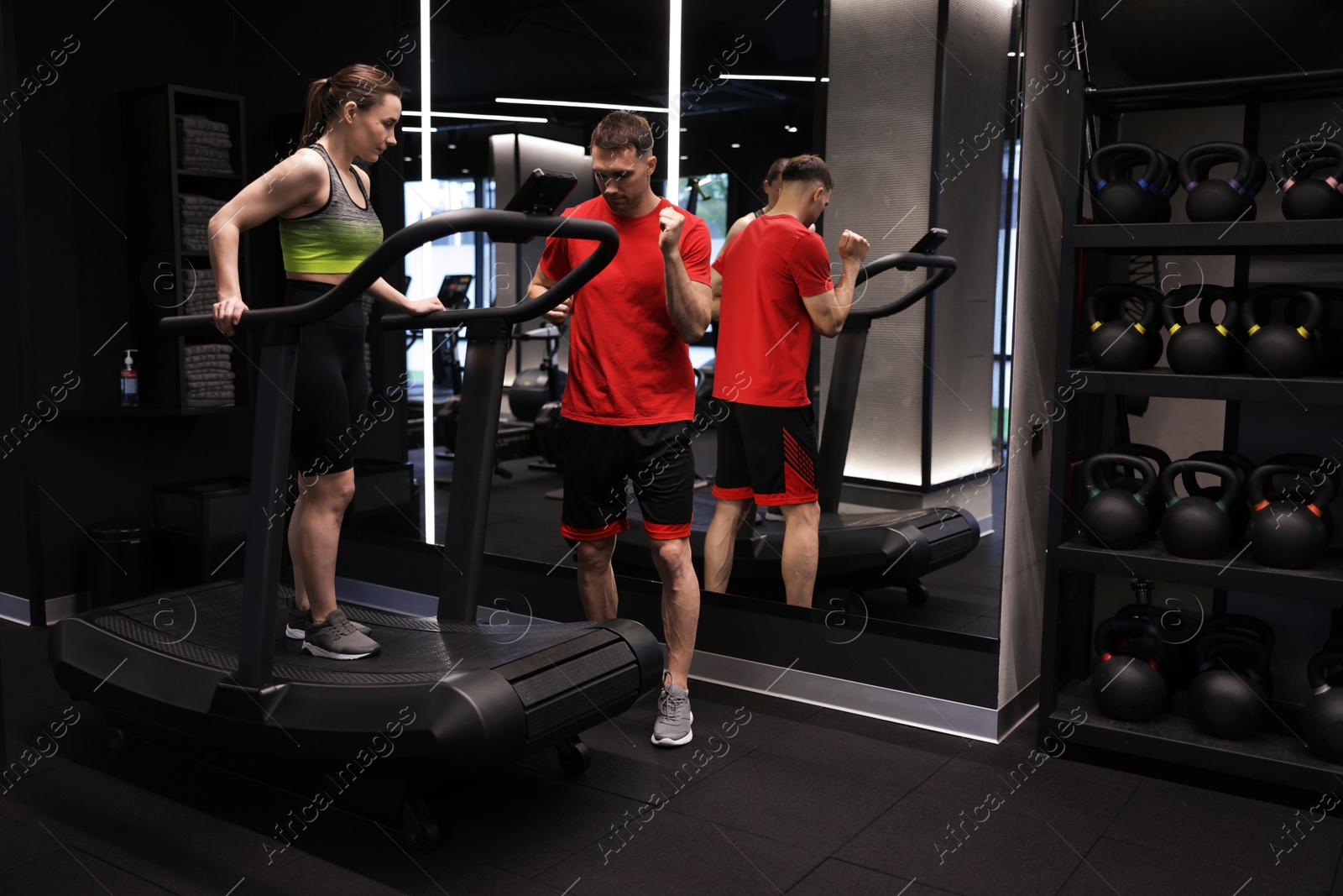 Photo of Young woman exercising on treadmill with professional personal trainer in gym