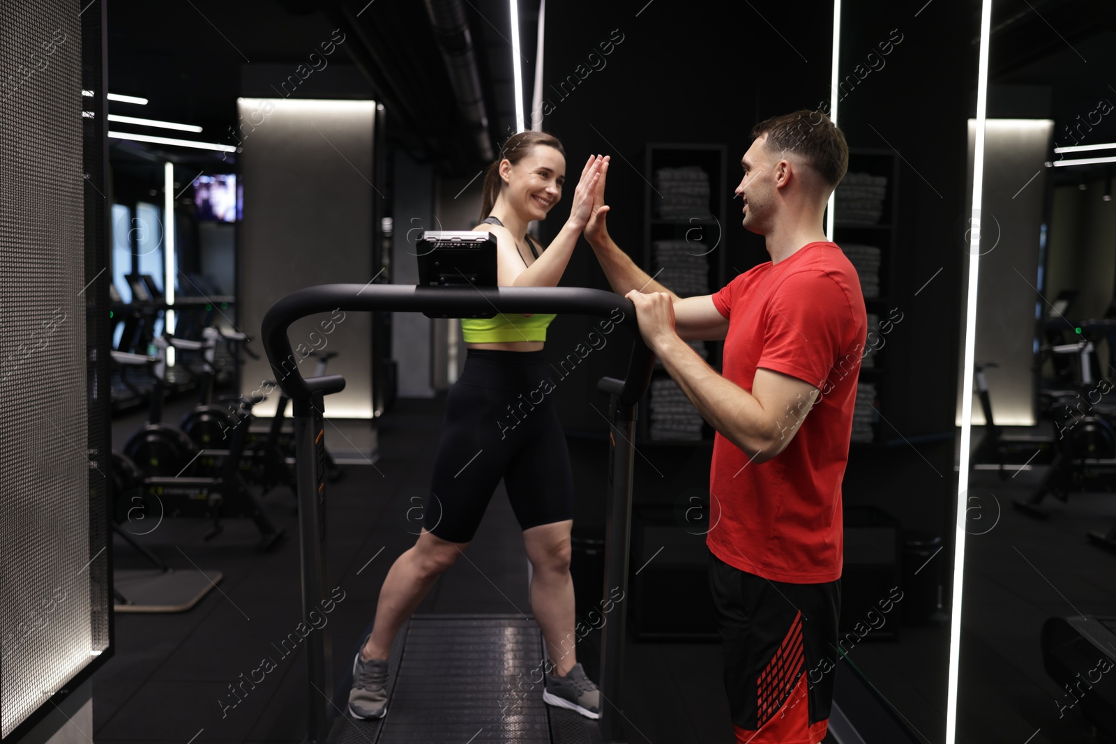 Young woman exercising on treadmill with professional personal trainer and giving high five in gym Photo of Young woman exercising on treadmill with professional personal trainer and giving high five in gym