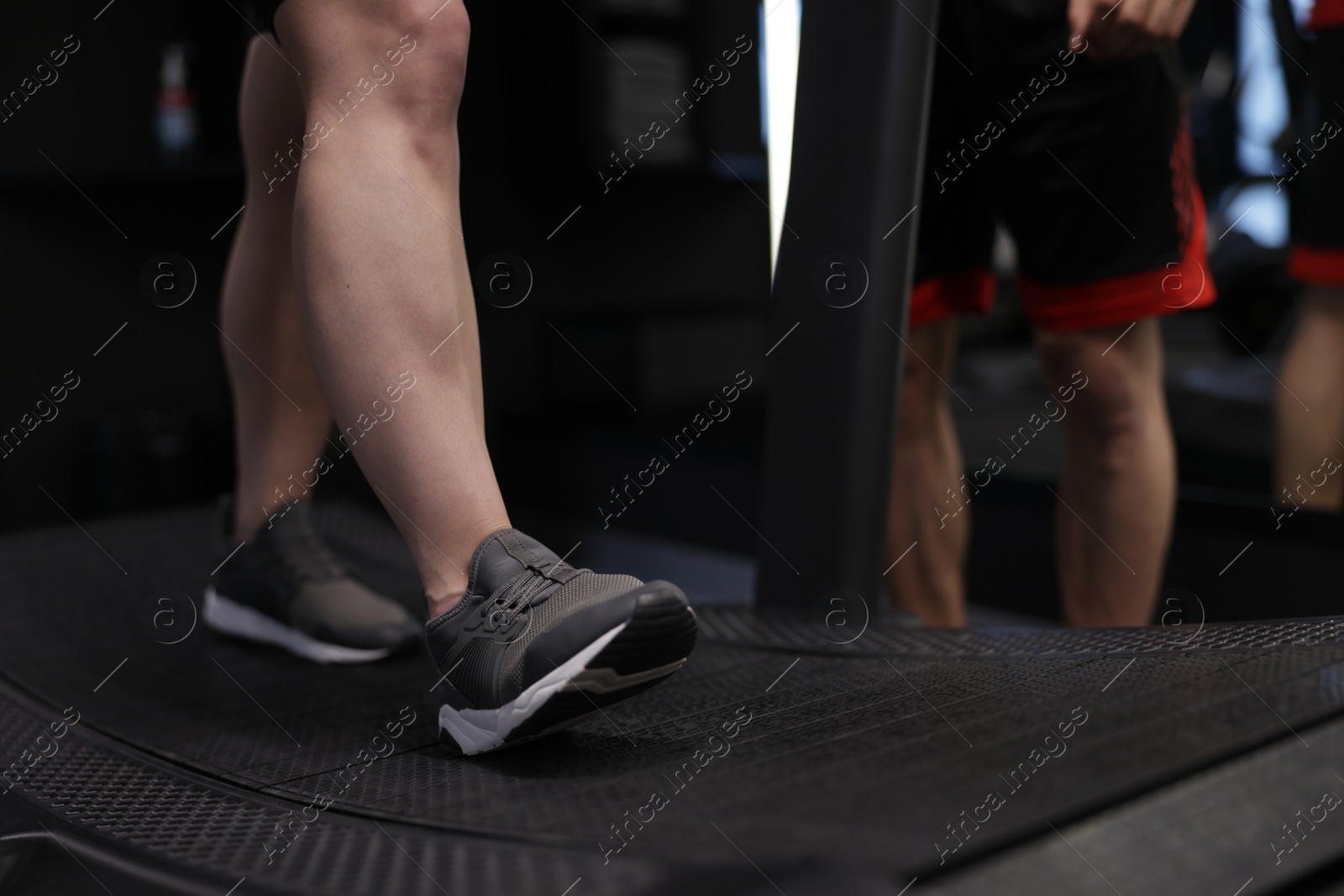 Photo of Young woman exercising on treadmill with professional personal trainer in gym, closeup