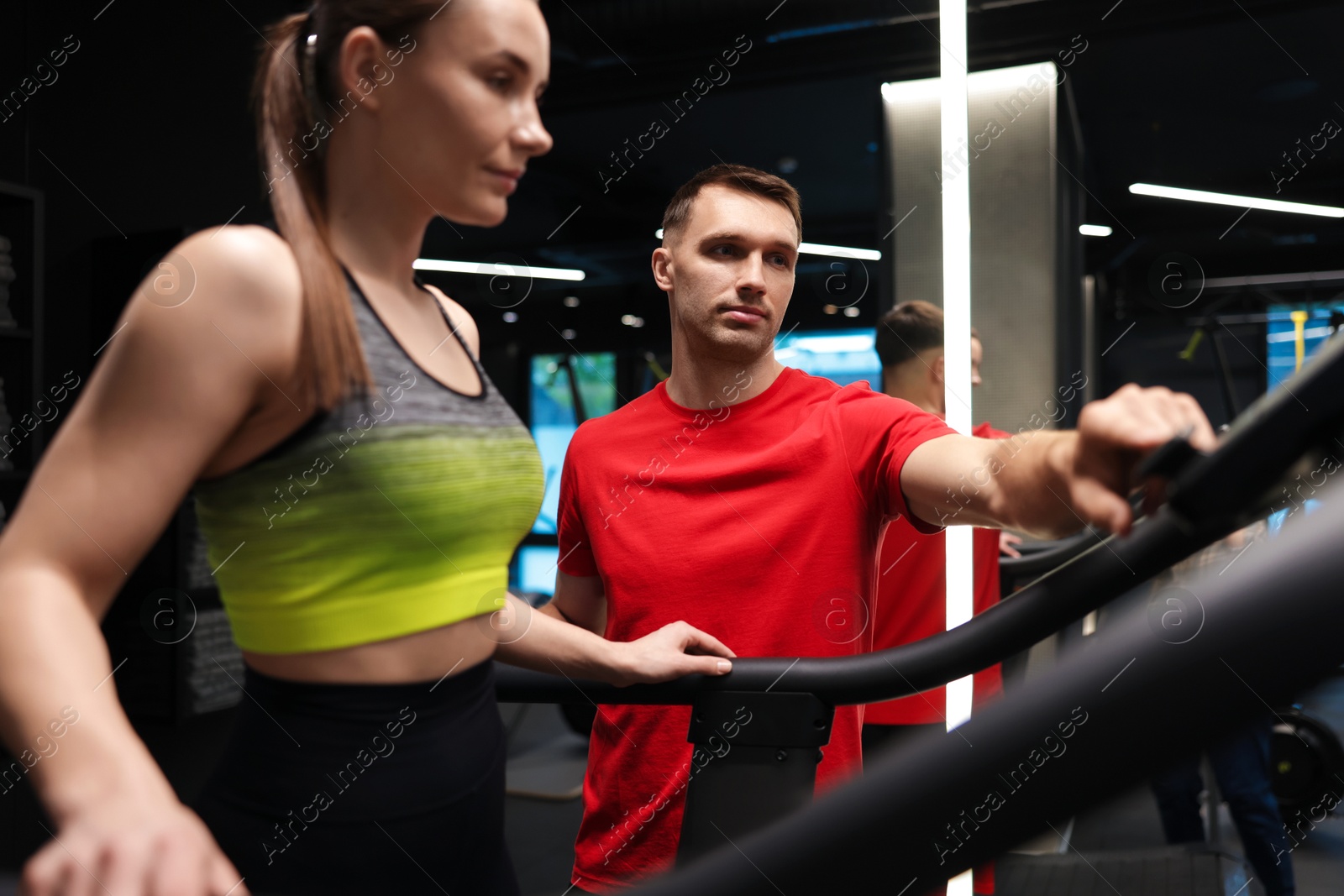 Young woman exercising on treadmill with professional personal trainer in gym Photo of Young woman exercising on treadmill with professional personal trainer in gym