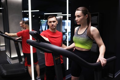 Photo of Young woman exercising on treadmill with professional personal trainer in gym