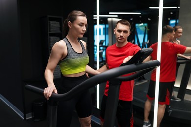 Photo of Young woman exercising on treadmill with professional personal trainer in gym