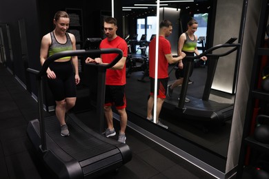Photo of Young woman exercising on treadmill with professional personal trainer in gym